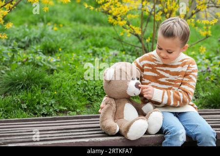 Bambina con orsacchiotto su una panchina di legno all'aperto. Spazio per il testo Foto Stock