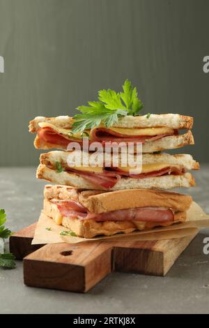 Pila di gustosi panini con prosciutto, prezzemolo e formaggio fuso su tavola grigia, primo piano Foto Stock