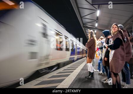 Foto di persone vestite in costume per il Carnevale di Colonia in piedi di fronte a un treno della S-Bahn di Colonia di notte che passa con effetto velocità. Foto Stock