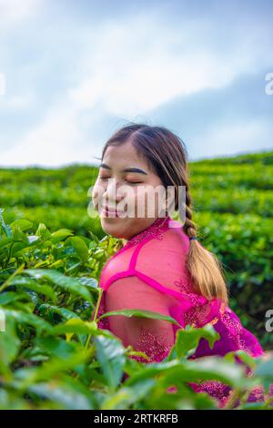 Una donna asiatica in un tradizionale costume rosa si trova in una piantagione di tè durante il giorno Foto Stock