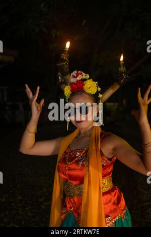 Un ballerino tradizionale indonesiano balla con occhiali da sole e un costume arancione con uno splendido scialle di notte Foto Stock