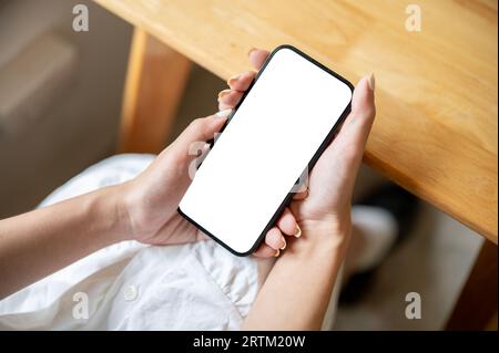 Immagine ravvicinata di un modello di smartphone con schermo bianco nelle mani di una donna. Una donna sta usando il suo telefono cellulare mentre è seduta a un tavolo in un bar. Foto Stock