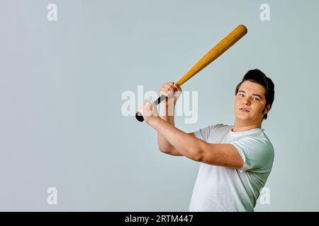 Un uomo con un pipistrello in mano oscilla su uno sfondo grigio Foto Stock
