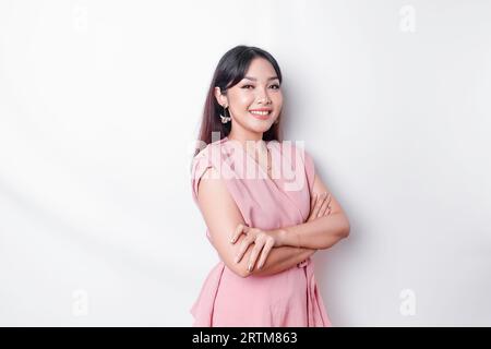 Ritratto di una donna asiatica sorridente e sicura di sé vestita di rosa, in piedi con le braccia piegate e guardando la fotocamera isolata su sfondo bianco Foto Stock