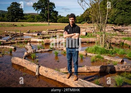 Ben Eardley, Project Manager National Trust, si trova su uno dei centinaia di tronchi collocati sulla nuova pianura alluvionale del fiume Aller, sulla National Trust Holnicote Estate, Exmoor, Somerset, dove il primo tentativo su larga scala di creare un ambiente più naturale, le zone umide e il paesaggio diversificate e resilienti nel Regno Unito contribuiranno ad affrontare gli impatti dei cambiamenti climatici, come le inondazioni e la siccità. Data foto: Mercoledì 13 settembre 2023. Foto Stock