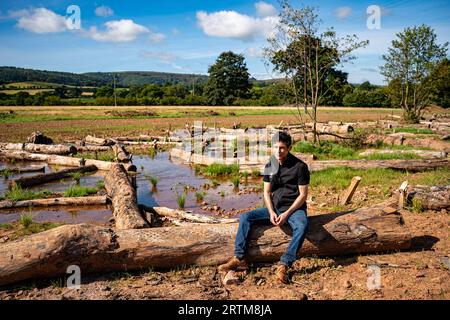 Ben Eardley, Project Manager National Trust, si trova su uno dei centinaia di tronchi collocati sulla nuova pianura alluvionale del fiume Aller, nella tenuta Holnicote del National Trust, a Exmoor, nel Somerset, dove il primo tentativo su larga scala di creare un ambiente più naturale, le zone umide e il paesaggio diversificate e resilienti nel Regno Unito contribuiranno ad affrontare gli impatti dei cambiamenti climatici, come le inondazioni e la siccità. Data foto: Mercoledì 13 settembre 2023. Foto Stock