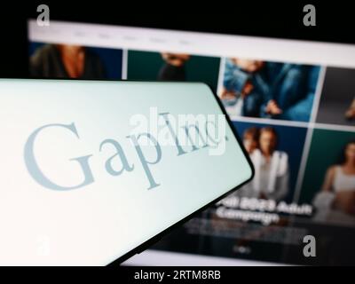 Telefono cellulare con logo della società statunitense di abbigliamento e accessori Gap Inc. Sullo schermo davanti al sito Web. Mettere a fuoco il display centrale sinistro del telefono. Foto Stock