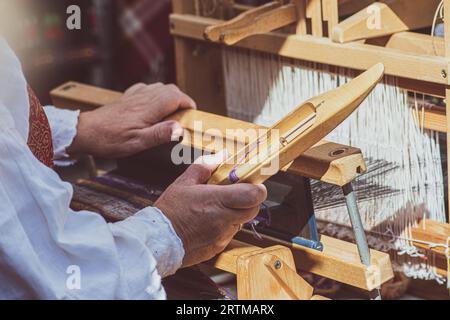 Una artigiana che lavora su un'antica tessitura in legno, indossa abiti tradizionali in una fiera di arte e artigianato a Vilnius, Lituania Foto Stock