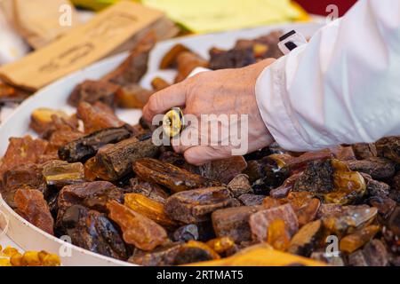 Mano di una donna che sceglie l'ambra tra molti pezzi ruvidi di ambra di colori diversi in un mercato di strada Foto Stock