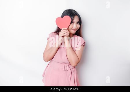 Simpatica e timida ragazza asiatica che arrossisce, dando una carta rossa a forma di cuore, sfondo bianco isolato Foto Stock