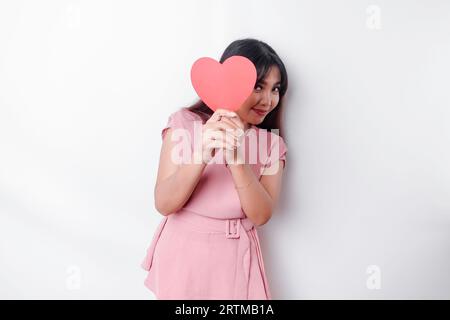 Simpatica e timida ragazza asiatica che arrossisce, dando una carta rossa a forma di cuore, sfondo bianco isolato Foto Stock