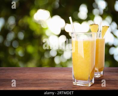 Gustoso frullato di ananas in bicchieri su tavolo in legno su sfondo sfocato, spazio per il testo Foto Stock