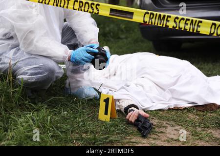 Criminologo che scatta foto di cadaveri sulla scena del crimine all'aperto, primo piano Foto Stock