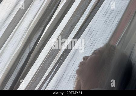 Triste giovane donna in piedi dietro le tende vicino alla finestra. Ho chi Minh. Vietnam. Foto Stock