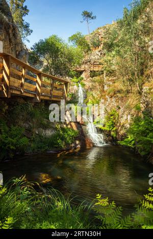 Splendida cascata di Penedo Furado a Vila de Rei, Portogallo, con una piscina naturale circondata da vegetazione e sentieri in legno. Foto Stock