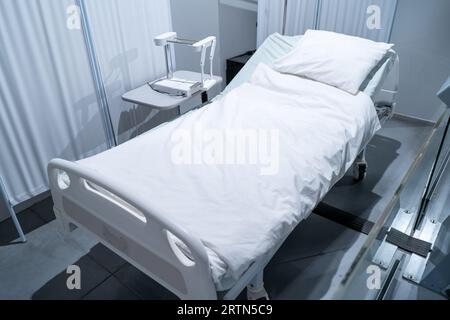 Letto bianco in una stanza d'ospedale. Coperta e cuscino. Interno di una stanza d'ospedale vuota. Foto Stock