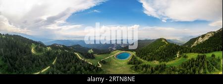 Vista panoramica aerea con drone di Poiana Brasov, Romania. Lago situato in cima alla montagna coperta da una lussureggiante foresta, città in lontananza Foto Stock