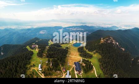 Vista panoramica aerea con drone di Poiana Brasov, Romania. Lago e altri edifici situati in cima alla montagna ricoperti da una lussureggiante foresta, città nel Foto Stock