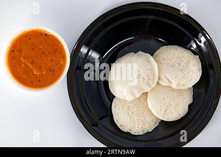 Cuocere e cuocere a vapore in un piatto nero e chutney di pomodoro su uno sfondo bianco isolato. Cottura a vapore a caldo a freddo e chutny rosso isolato. Cibo sano / B Foto Stock