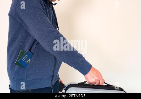 Uomo civile in felpa blu con passaporto ucraino straniero in tasca con valigia da viaggio in mano Foto Stock