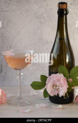 Bicchiere di champagne rosa con fiori di rosa su sfondo grigio chiaro Foto Stock