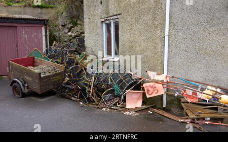 Un mucchio di attrezzatura da pesca, un rimorchio con pneumatici sgonfi e rifiuti allineati accanto a un muro nel porto di St Abbs Foto Stock