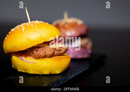 Mini hamburger gourmet colorati con semi di sesamo su tavola di ardesia nera Foto Stock