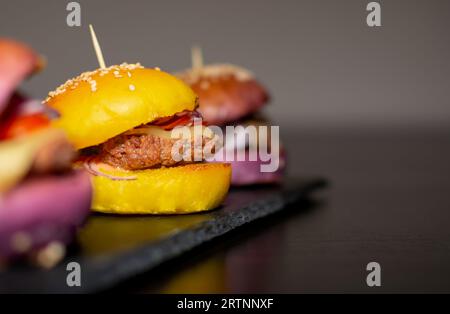 Mini hamburger gourmet colorati con semi di sesamo su tavola di ardesia nera Foto Stock