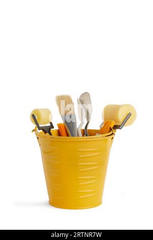 Dipingere pennelli, rulli e spatole in un secchio di metallo giallo su sfondo bianco con spazio per la copia Foto Stock