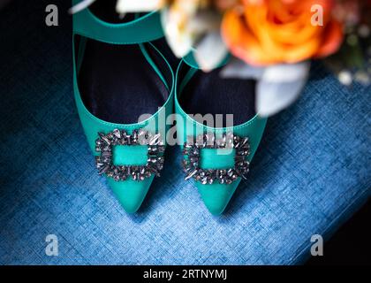 Bellissime scarpe da sposa con tacco a spillo verde con fibbia diamantata e bouquet di fiori d'arancio. Seduto sul sedile blu, colori incredibili Foto Stock