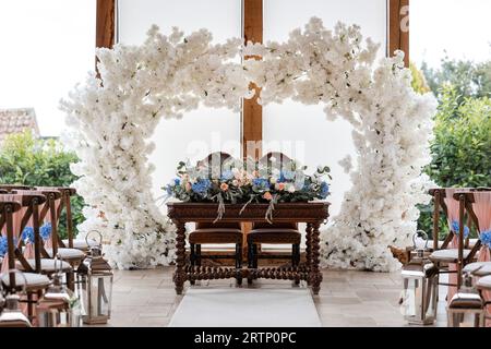 Splendidi posti a sedere per matrimoni con arco a fiori e posti in legno. Decorazione e sfondo romantico. Foto Stock