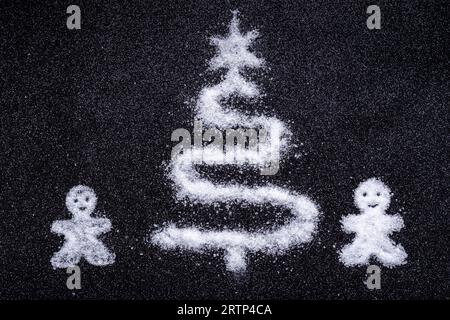 Silhouette di un albero di Natale e omini fatti di sale come la neve su sfondo nero. Un creativo biglietto d'auguri invernale fatto in casa Foto Stock
