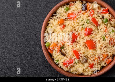 Delizioso porridge di couscous con cubetti di verdure grigliate con sale e spezie su uno sfondo di cemento scuro Foto Stock