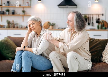 Sostegno, simpatia.Sad sposi caucasici maturi sedersi sul divano a casa, il marito rassicura la moglie, empatizza con lei, sostiene, chiede perdono, la moglie sperimenta problemi personali, è offeso Foto Stock