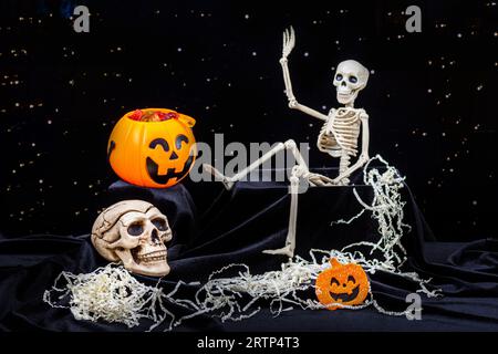 Uno scheletro giocattolo che strisciava fuori dalla tomba, e agitava la mano, saluta, zucche con grimaci, un teschio su sfondo nero. Alla vigilia del giorno di de Foto Stock