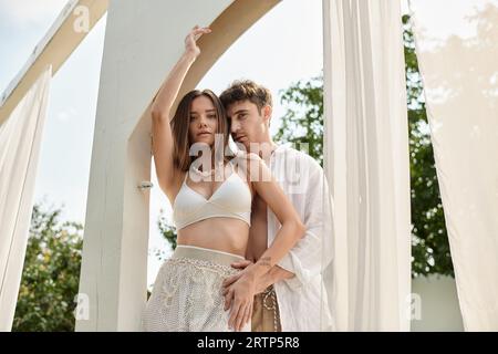 bell'uomo e una bella donna in piedi vicino al padiglione della spiaggia con tulle bianco, coppia romantica Foto Stock