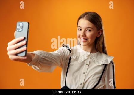 Ragazza adolescente che fa un selfie sul suo telefono su sfondo giallo Foto Stock