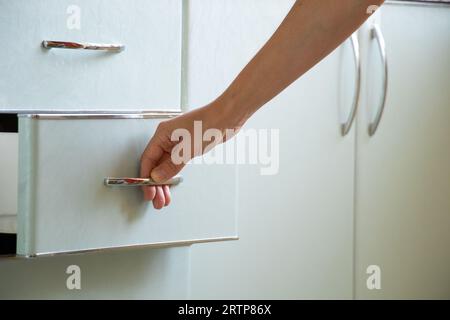 La mano della donna apre l'armadio da cucina sotto la luce del sole, i mobili da cucina a casa Foto Stock