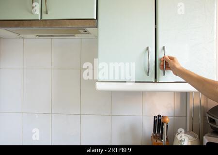 La mano della donna apre l'armadio da cucina sotto la luce del sole, i mobili da cucina a casa Foto Stock