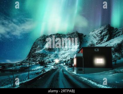 Fantastico scenario di Aurora borealis o di aurora boreale che ballano sulle montagne innevate nel villaggio scandinavo in inverno alle isole Lofoten, Norvegia Foto Stock