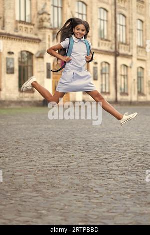 felice di saltare la ragazza della scuola con lo zaino. studentessa di salto all'aperto. foto di una studentessa che salta. bruna a scuola che salta. Foto Stock