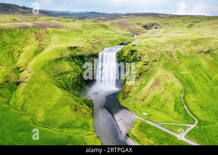 Vista aerea della maestosa cascata Skogafoss che scorre dalla scogliera circondata da un paesaggio lussureggiante in estate in Islanda. Famose attrazioni turistiche e di campagna Foto Stock