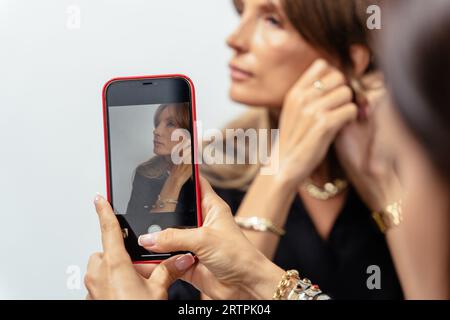 Ritratto di attraente blogger donna matura in modello nero con bracciali dorati, anelli, catene su sfondo bianco. Foto Stock