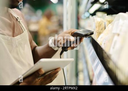 Primo piano di un lavoratore di supermercati afroamericano che utilizza un tablet pc per scansionare i codici delle merci sugli scaffali Foto Stock