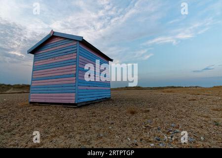 Una capanna sulla spiaggia rosa e blu che si erge da sola su una spiaggia con dune dietro e un'ampia distesa di cielo su una spiaggia di Norfolk Foto Stock