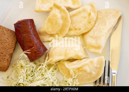 Gnocchi con patate e una salsiccia fritta e insalata di cavolo su un piatto bianco per pranzo, mangia a casa Foto Stock