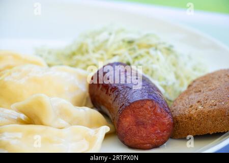 Gnocchi con patate e una salsiccia fritta e insalata di cavolo su un piatto bianco per pranzo, mangia a casa Foto Stock