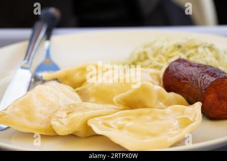 Gnocchi con patate e una salsiccia fritta e insalata di cavolo su un piatto bianco per pranzo, mangia a casa Foto Stock