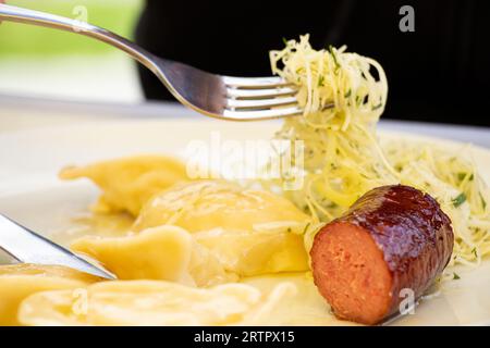 Gnocchi con patate e una salsiccia fritta e insalata di cavolo su un piatto bianco per pranzo, mangia a casa Foto Stock