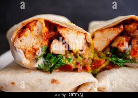 Vista ravvicinata di un Burrito Sofritas tagliato a metà: Burrito piccante di tofu ripieno di guacamole, panna acida vegan, coriandolo, lattuga, salsa, e pomodori Foto Stock